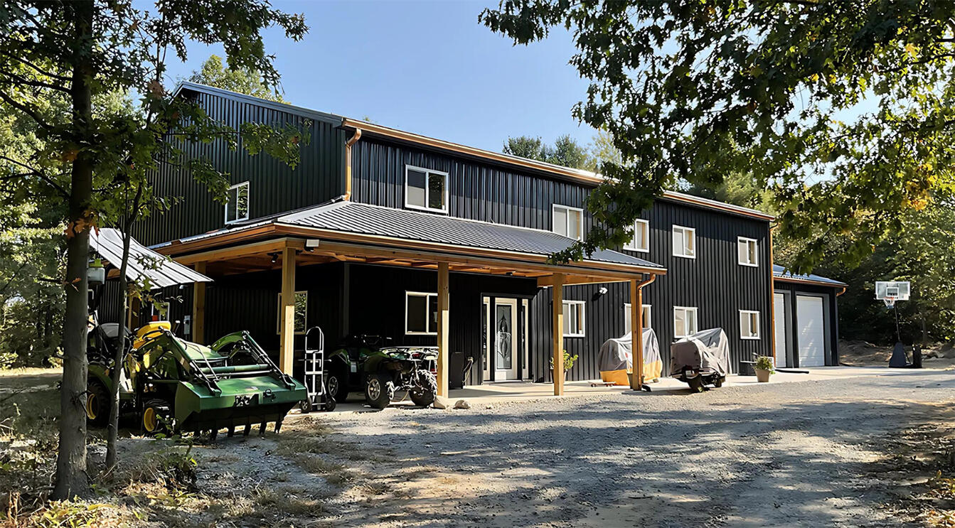 Black barndominium house surrounded by trees and vehicles Black barndominium house surrounded by trees and vehicles
